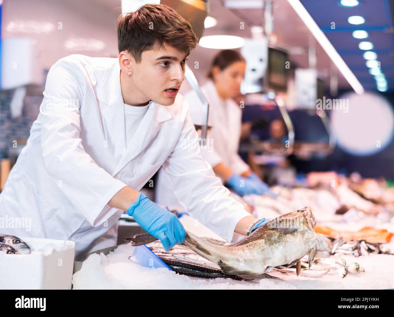 Positive salesman demonstrating cod in fish store Stock Photo - Alamy