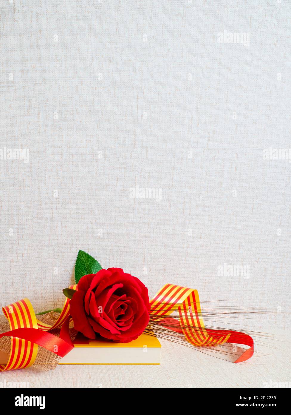 Sant jordi, rosa roja sobre libro amarillo con cintas con la bandera catalana y una cinta roja sobre fondo con textura Stock Photo