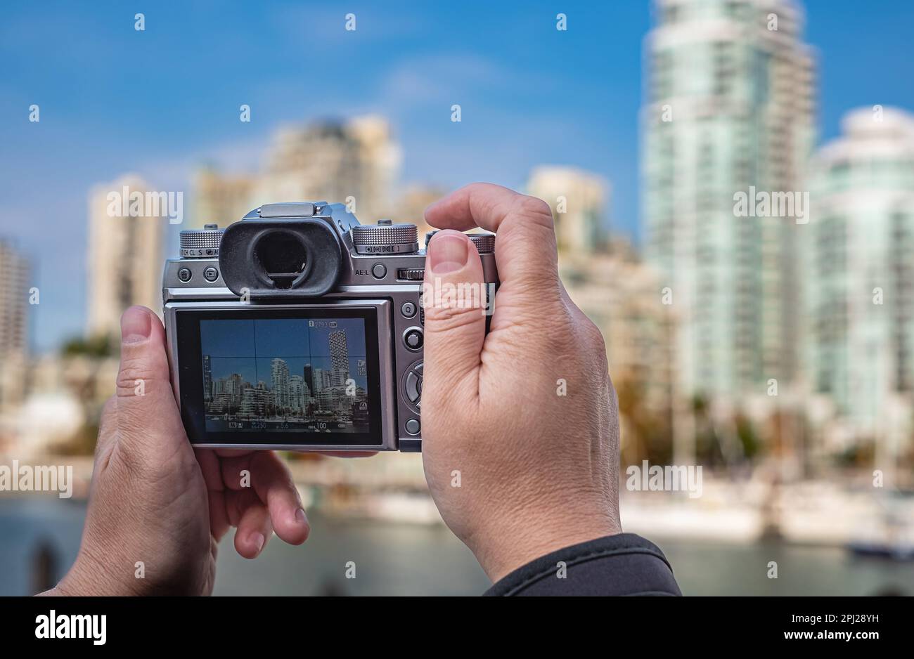 Photographer doing photos with still camera. Mirrorless camera in the hands of tourist taking photos of a city. Street view, travel photo, blurred bac Stock Photo