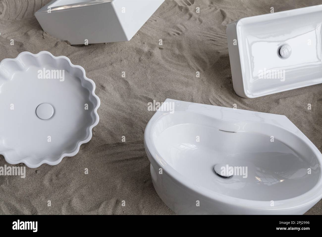Conceptual exposition of new designer white ceramic bathroom sinks for sale on a sand base. Stock Photo