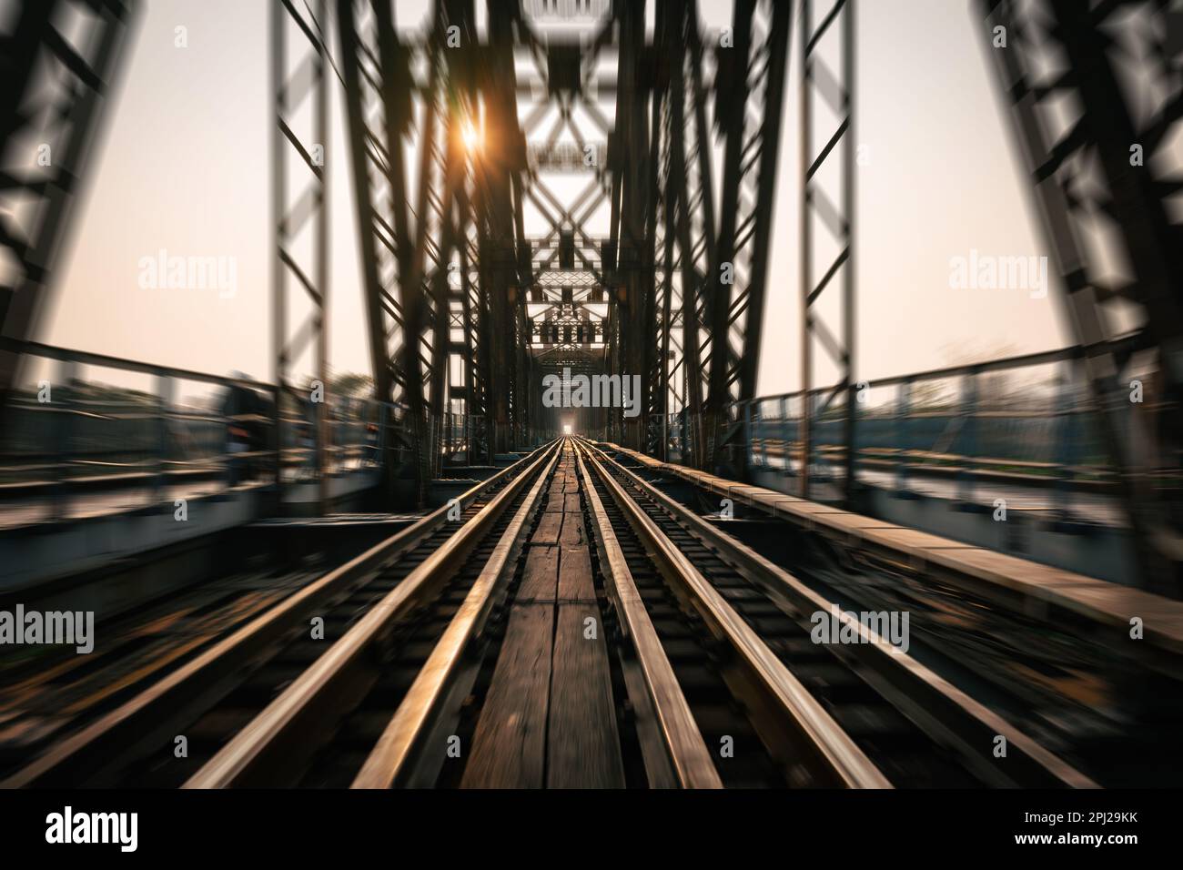 Train tracks lead downwards over a long metal bridge with a radial blur