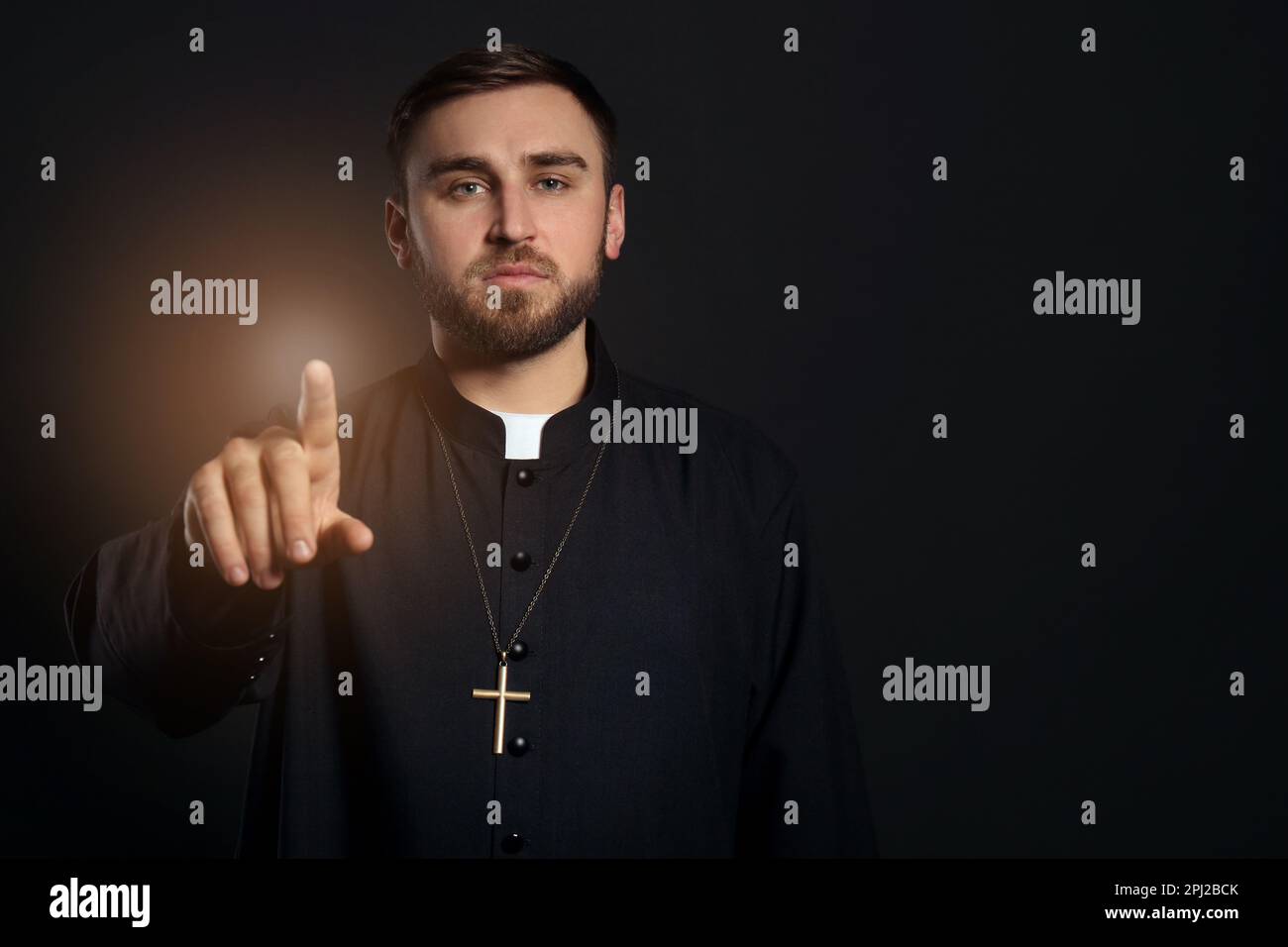Priest wearing cassock with clerical collar on black background. Space for text Stock Photo