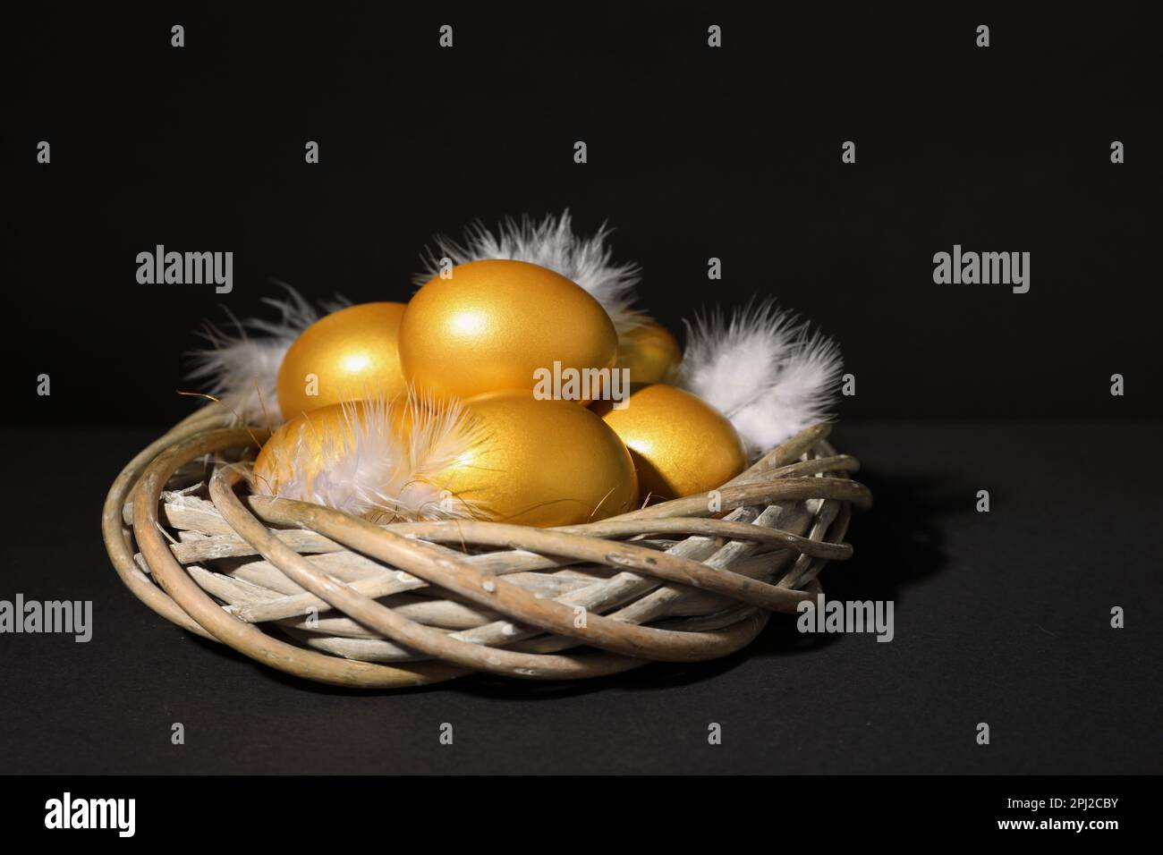 Shiny golden eggs with feathers in nest on black background Stock Photo ...