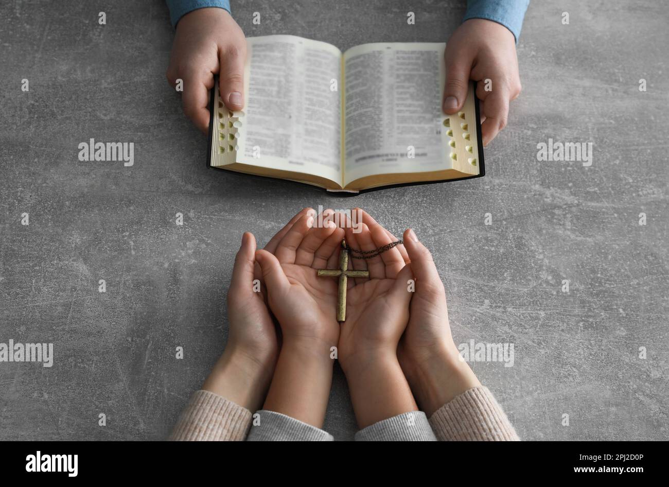 Boy praying and reading Bible with his godparents at grey table, closeup Stock Photo