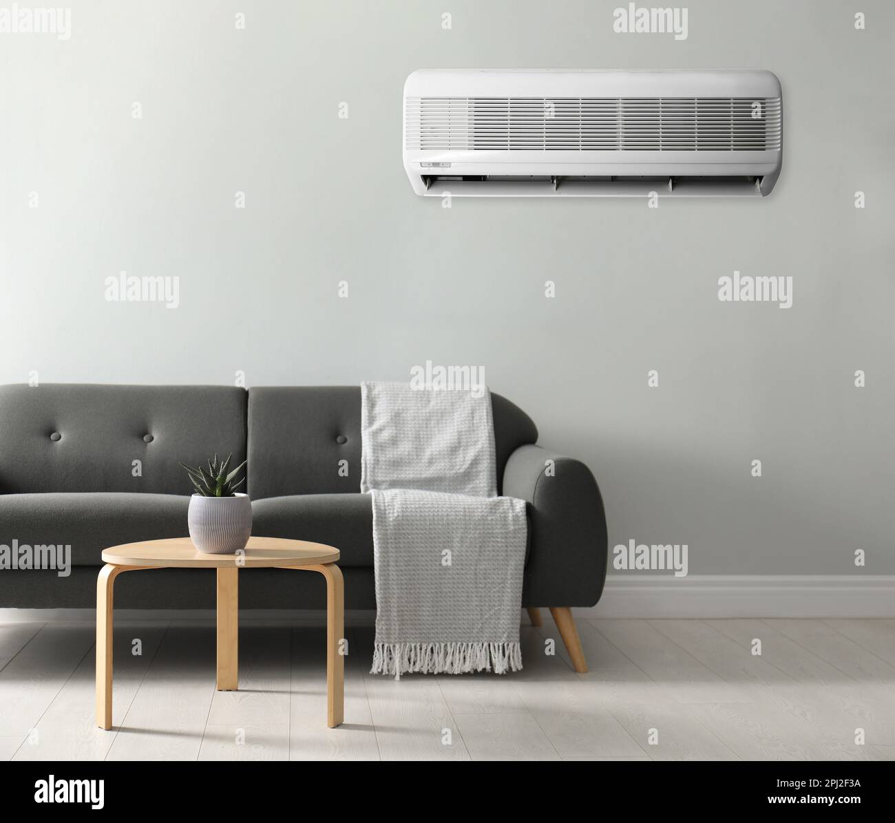 Modern air conditioner on white wall in room with stylish grey sofa ...