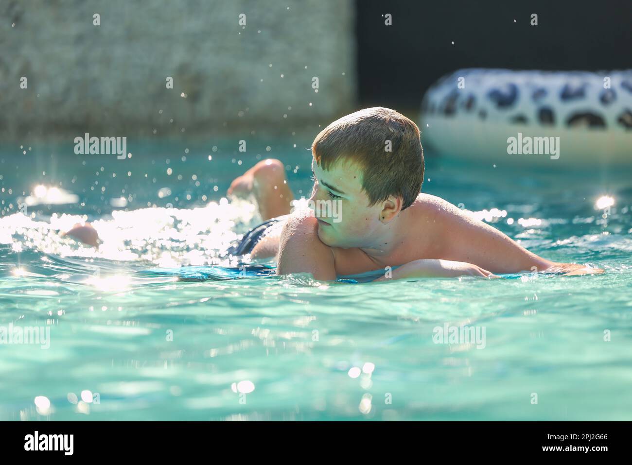 Adolescent boy swimming on boogie board in backyard pool Stock Photo