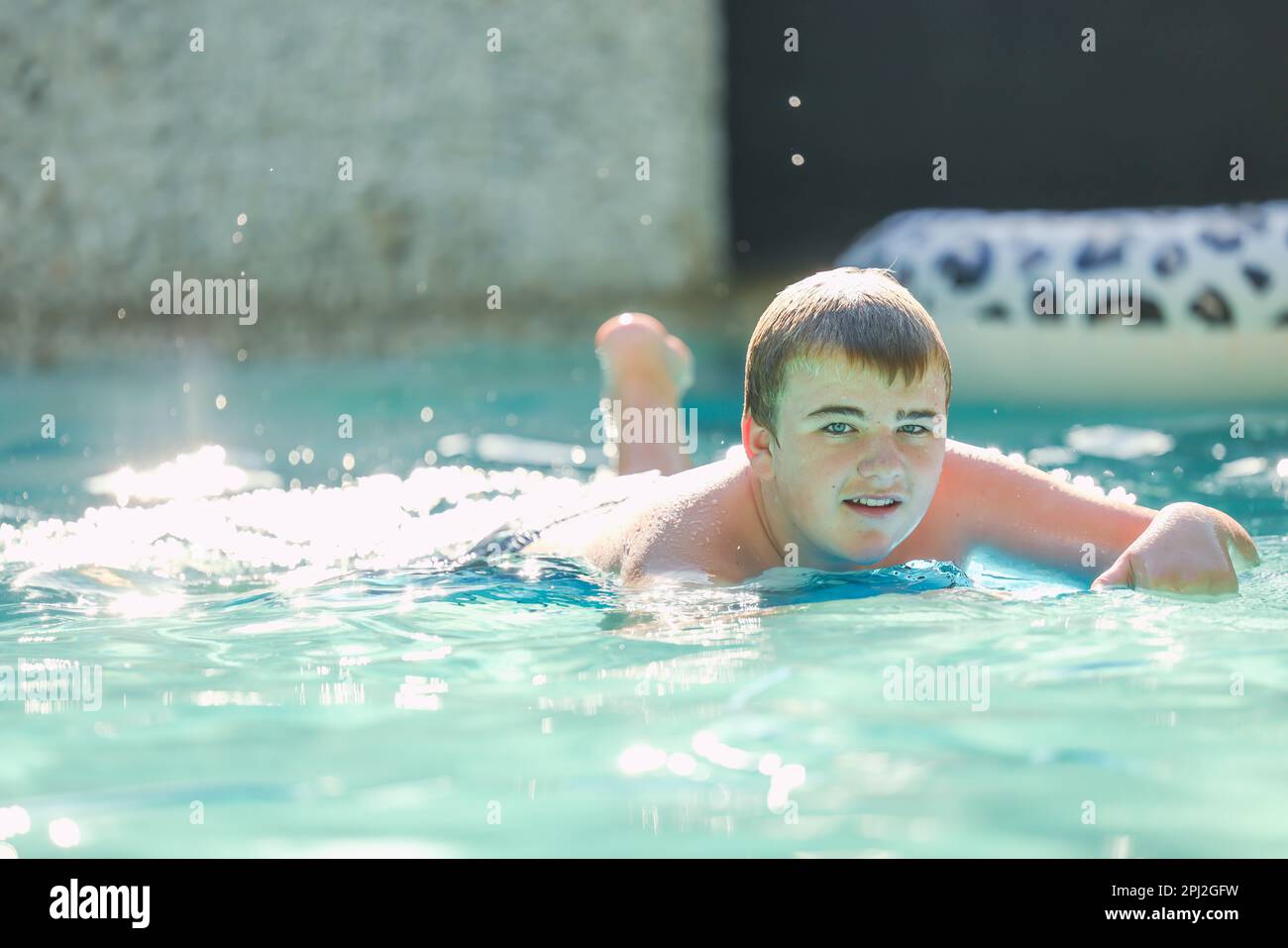 Adolescent boy swimming on boogie board in backyard pool Stock Photo