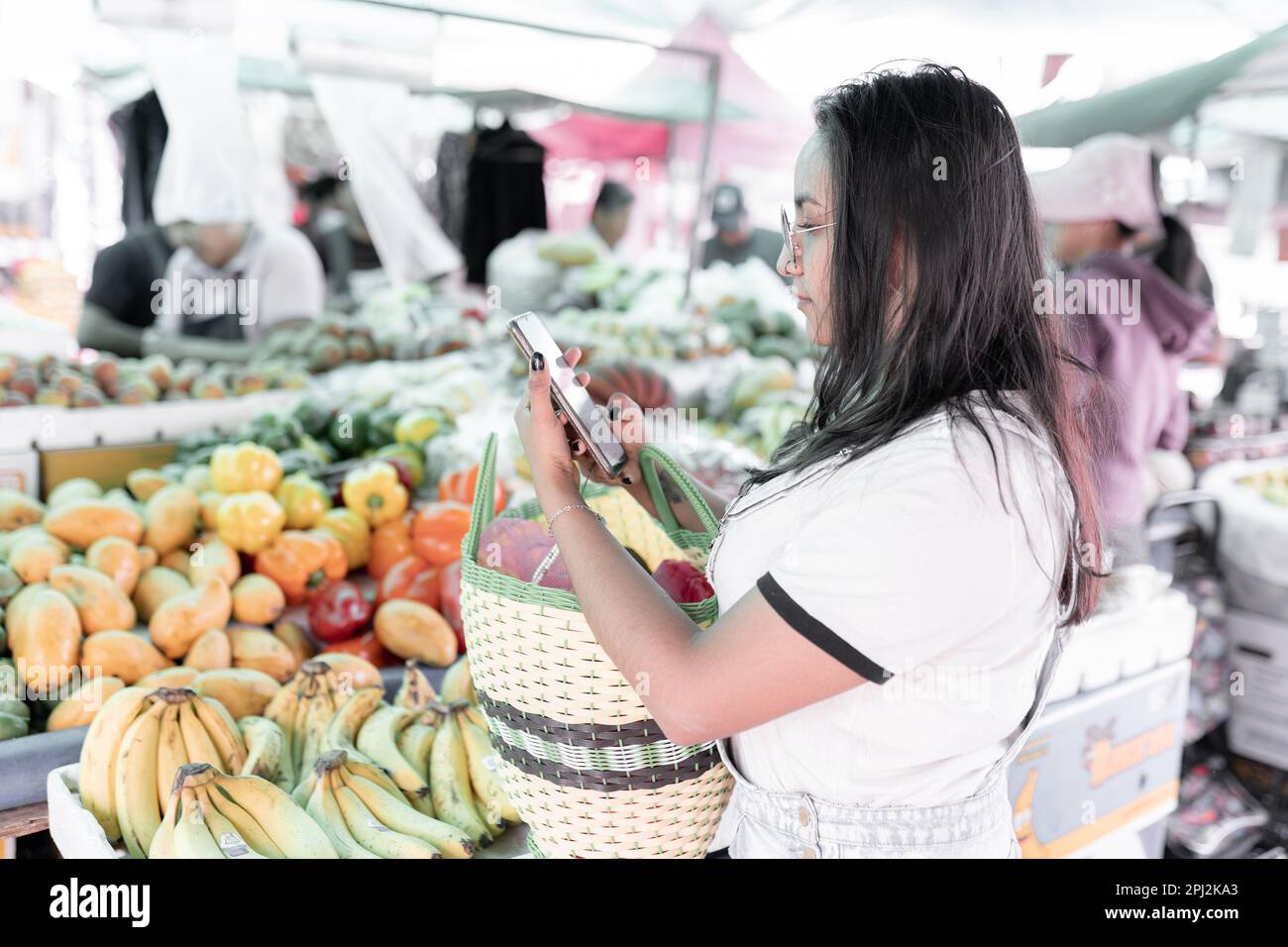 A young Hispanic woman is checking a shopping list in her phone in a street market Stock Photo