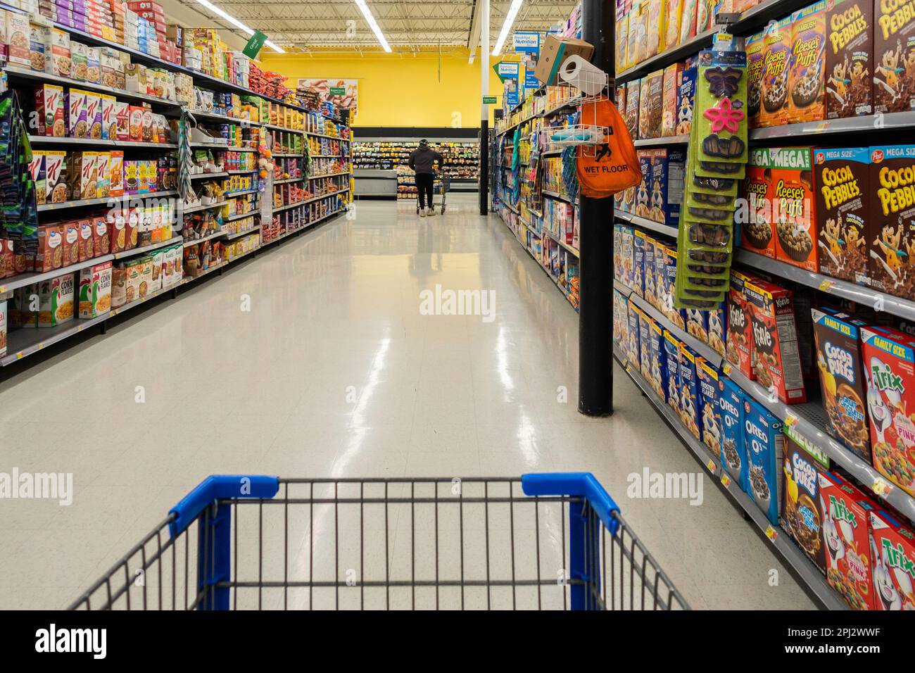 A distant man shopper walks down the boxed cereal aisle indoors at a Walmart Supercenter in Wichita, Kansas, USA. Stock Photo