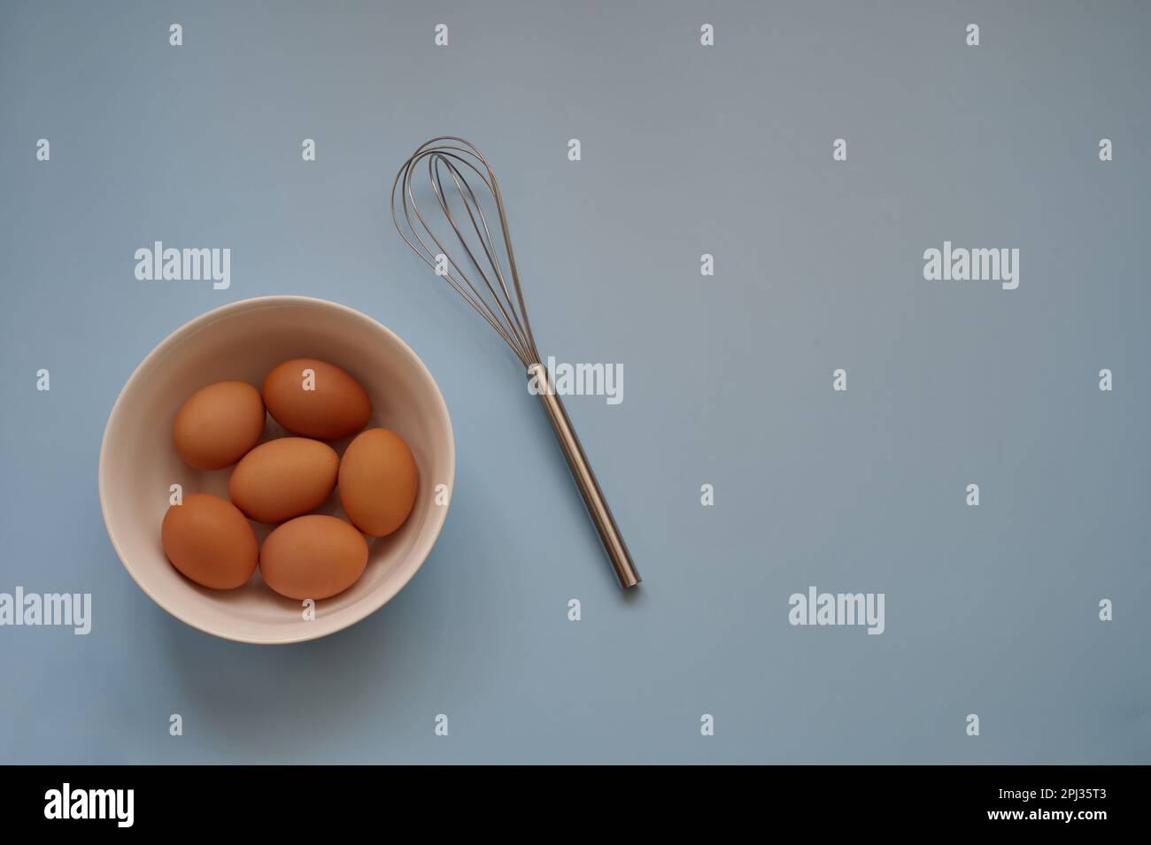 Eggs in white bowl and whisk on blue background - top view Stock Photo