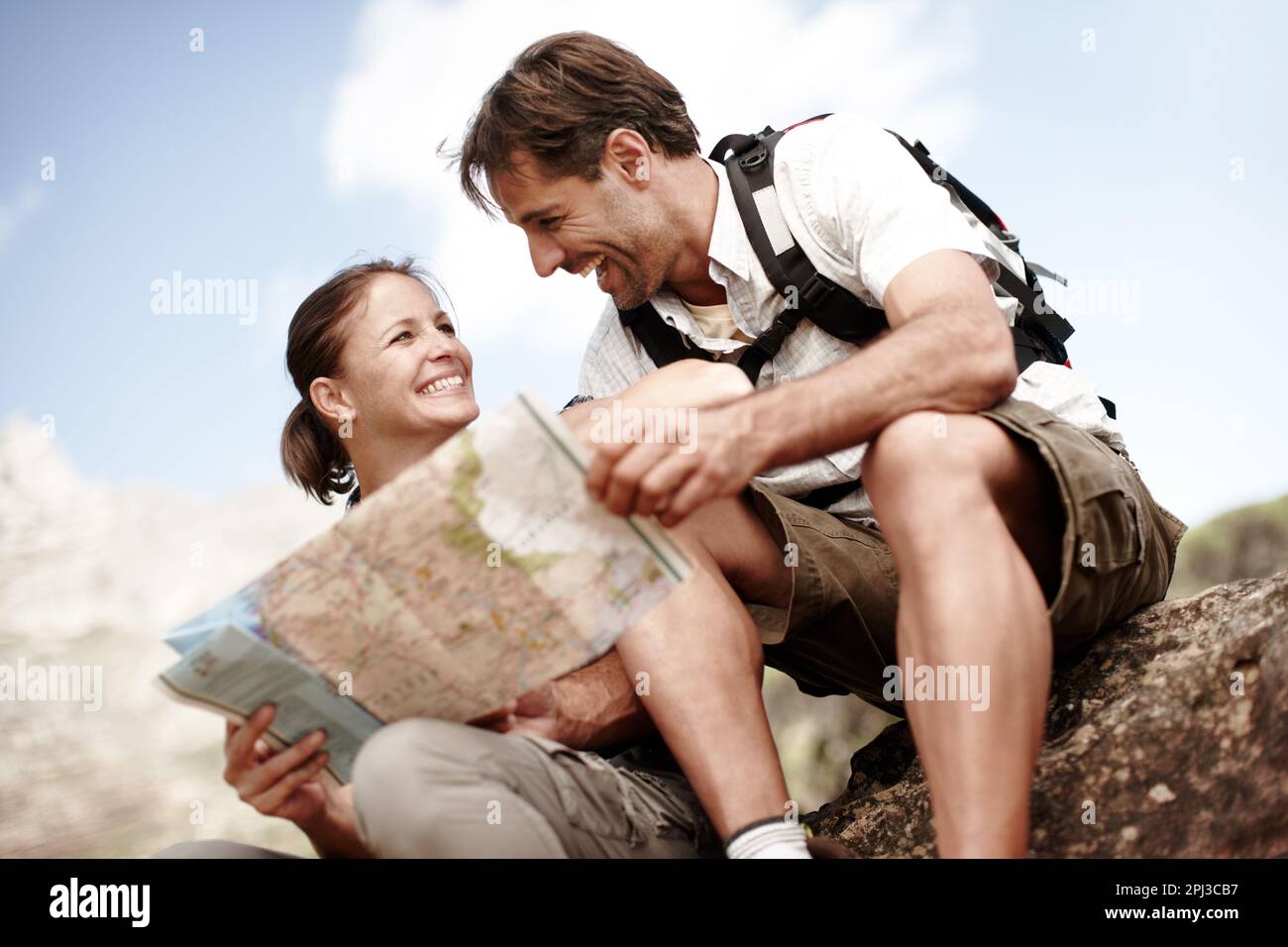 Which way should we go next. Two hikers consulting their map while sitting on a mountain top. Stock Photo