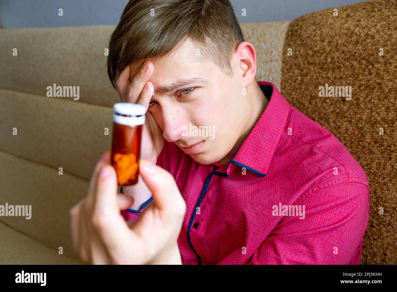 Unhappy Young Man get a Side Effect from a Pills on the Sofa in the Room Stock Photo