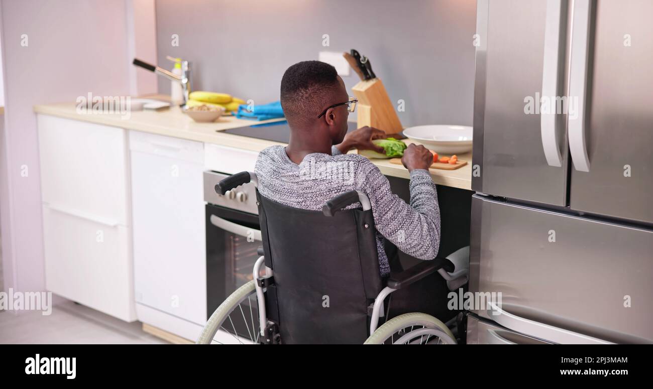 Young Disabled Man Sitting On Wheel Chair Preparing Food In Kitchen Stock Photo