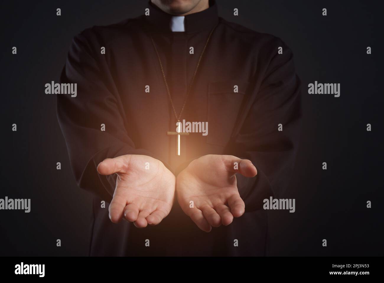 Priest reaching out his hands with holy light on black background, closeup Stock Photo