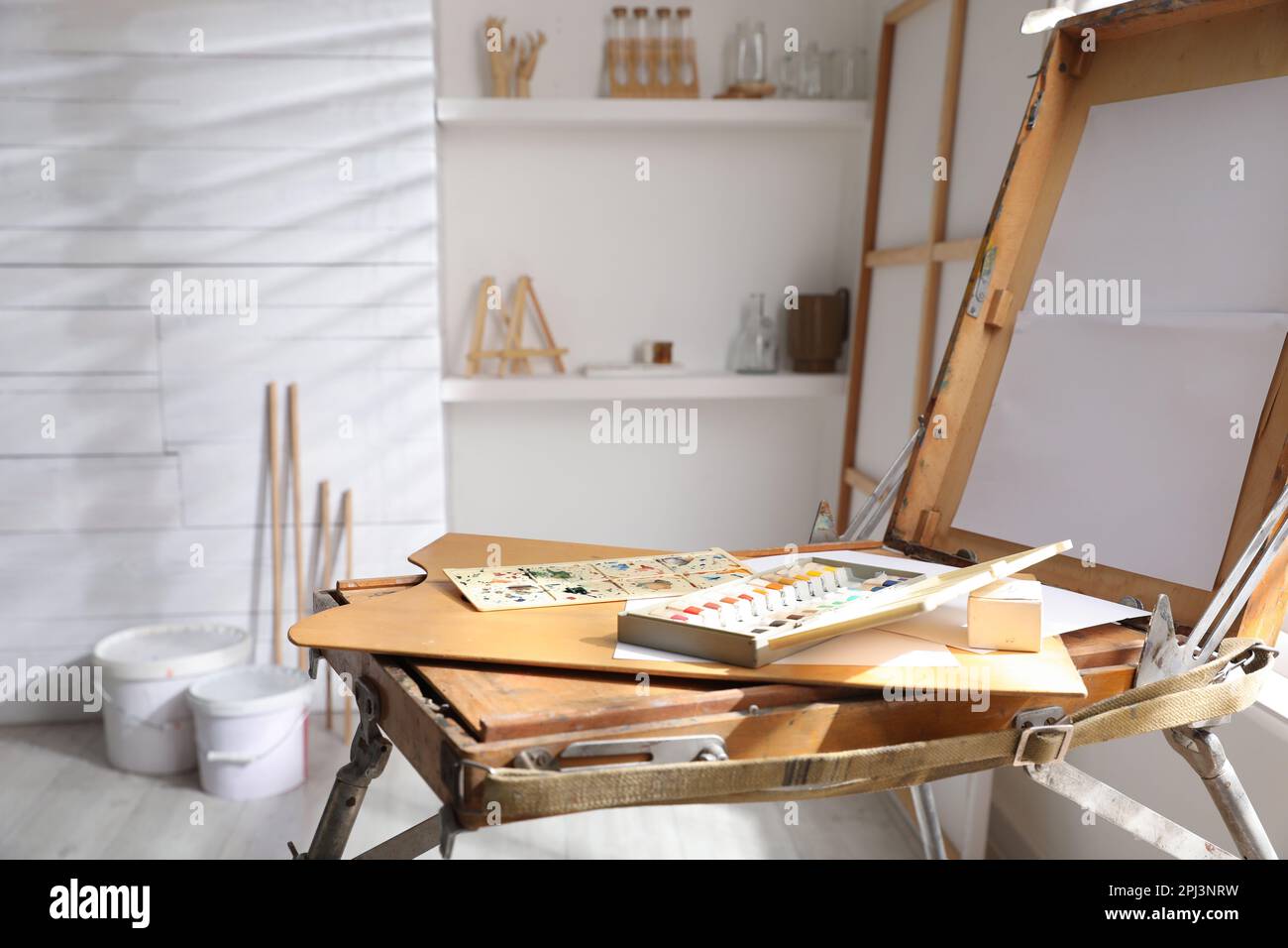 Foldable wooden easel with empty canvas and supplies in studio. Artist's workplace Stock Photo