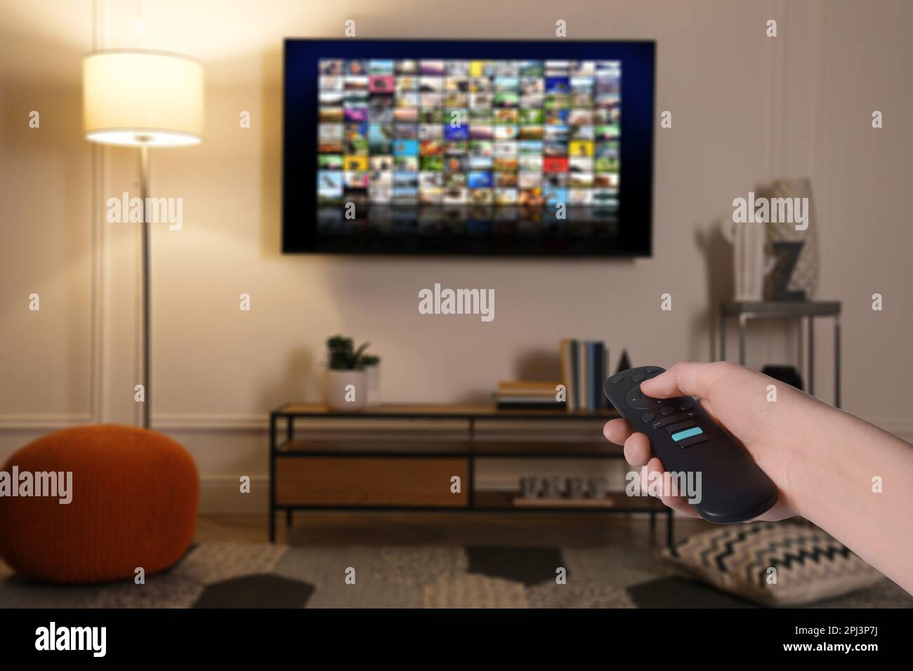 Woman with remote control changing channels while watching TV at home, closeup Stock Photo