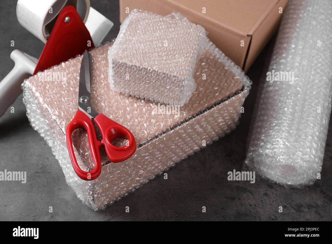 Cardboard boxes, bubble wrap, adhesive tape and scissors on dark grey