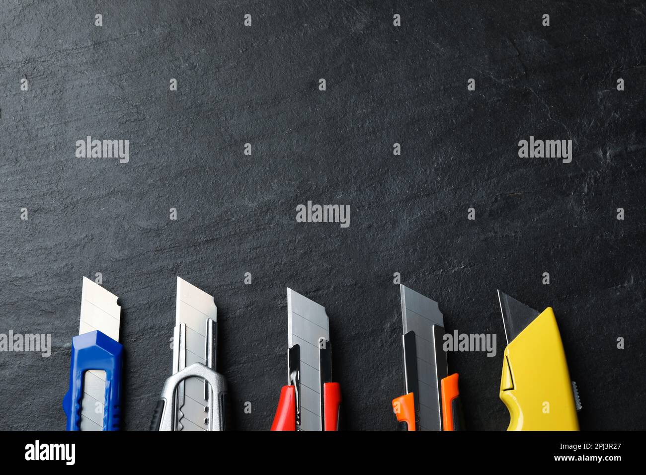 Different utility knives on black table, flat lay. Space for text Stock Photo