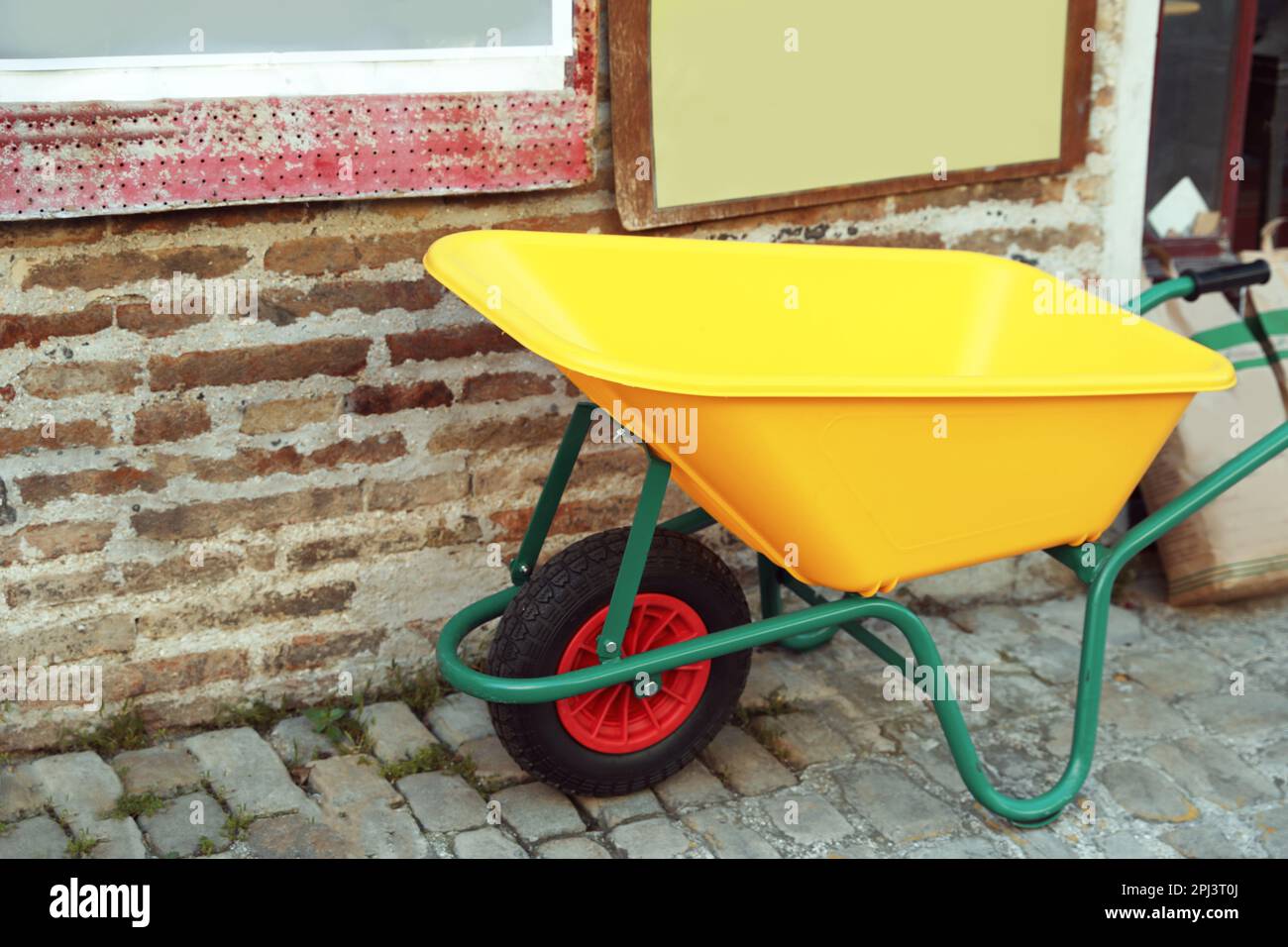 Bright yellow wheelbarrow near brick wall outdoors Stock Photo Alamy