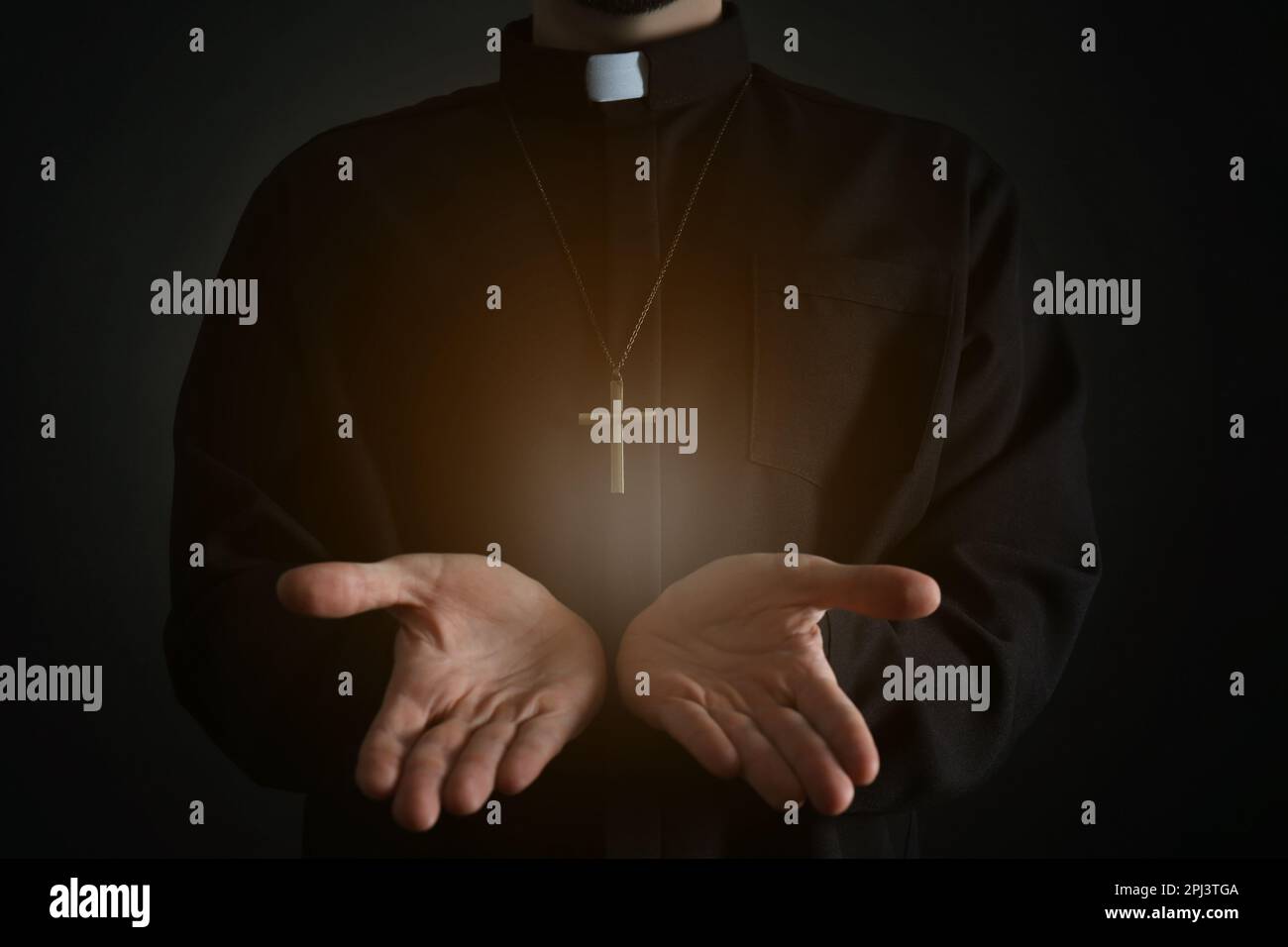 Priest reaching out his hands with holy light on dark background, closeup Stock Photo