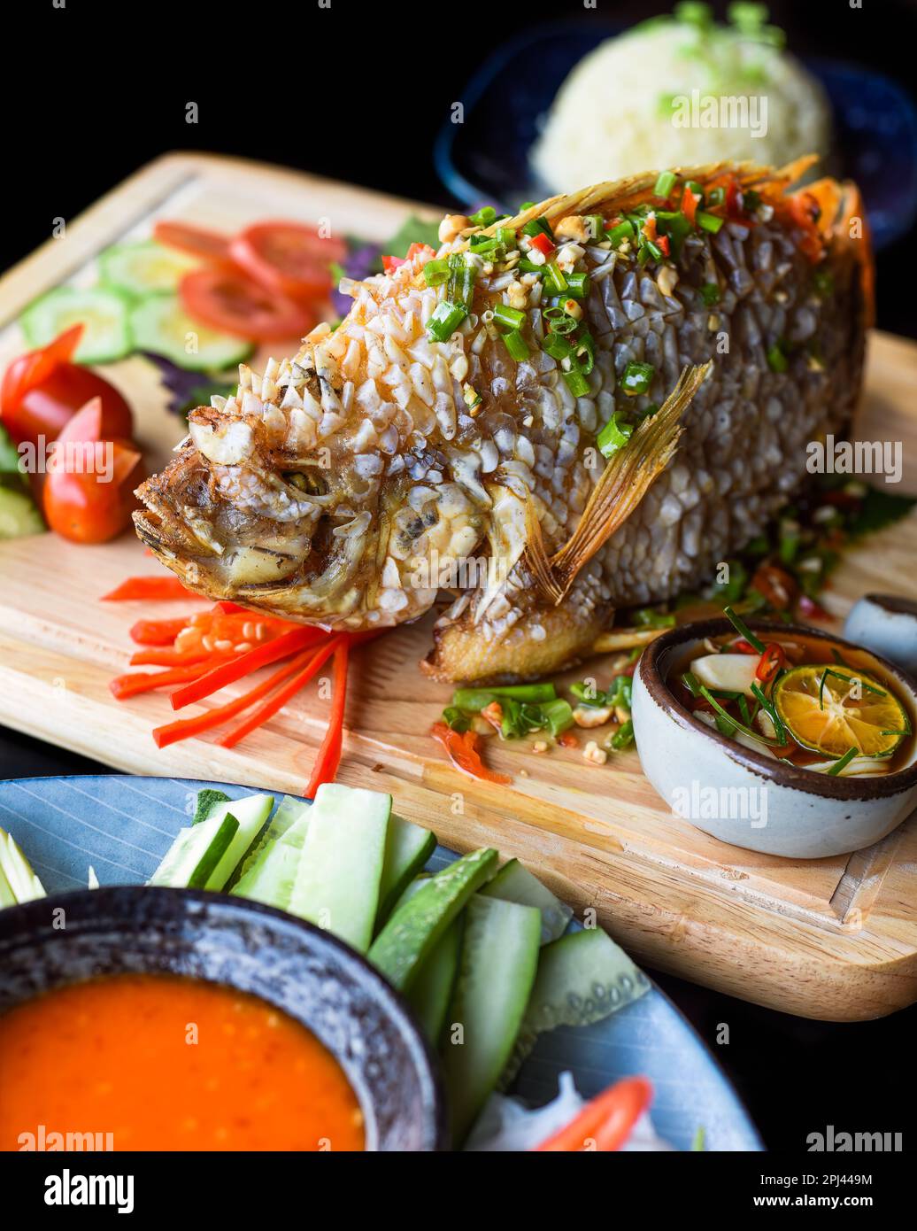 Red perch grilled in batter with vegetables and greens on wooden chop board isolated on black background side view Stock Photo