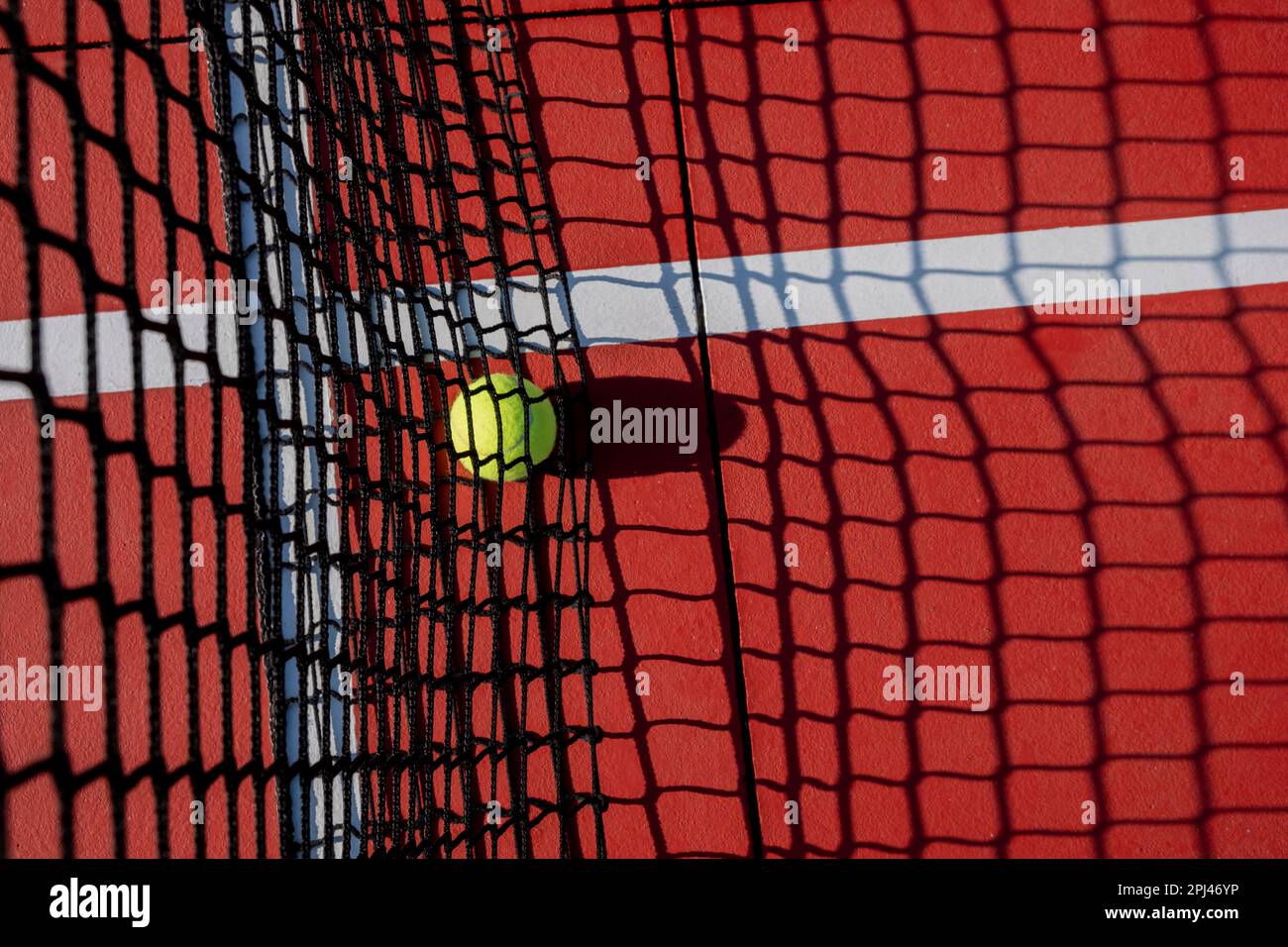 selective focus, a ball on the net of a red tennis court. Stock Photo