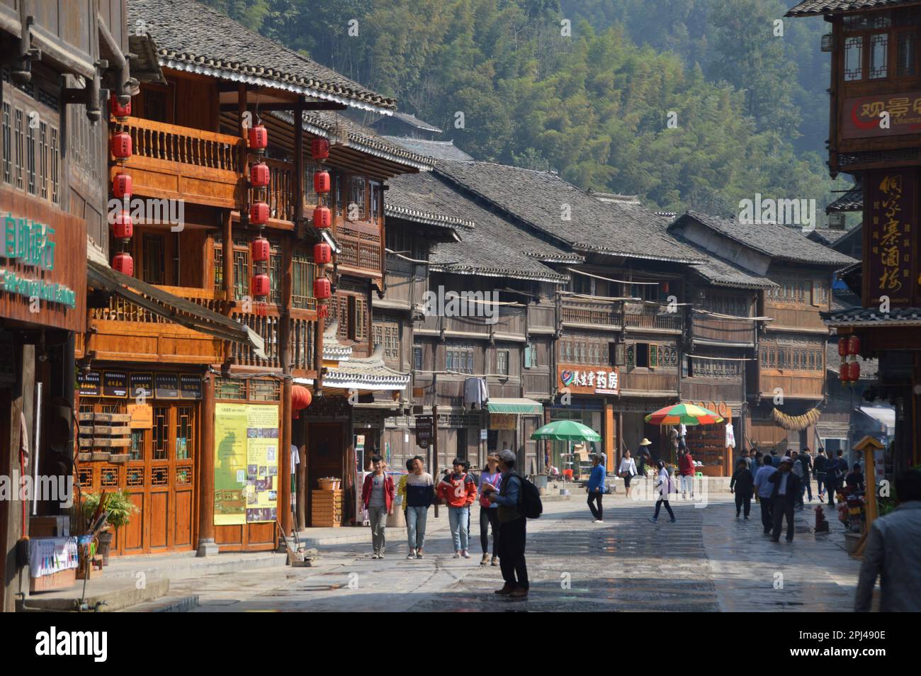 People's Republic of China, Guizhou Province,  Zhaoxing Dong Village:  historic wooden houses on the main street, with wooded hills behind. Stock Photo