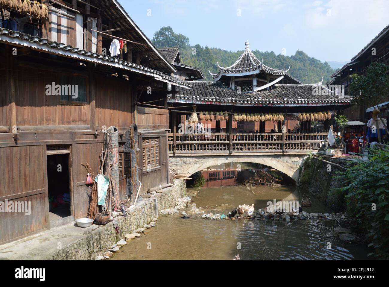 People's Republic of China, Guizhou Province,  Zhaoxing Dong Village:  view of the old wooden buildings from a bridge over the stream. Stock Photo