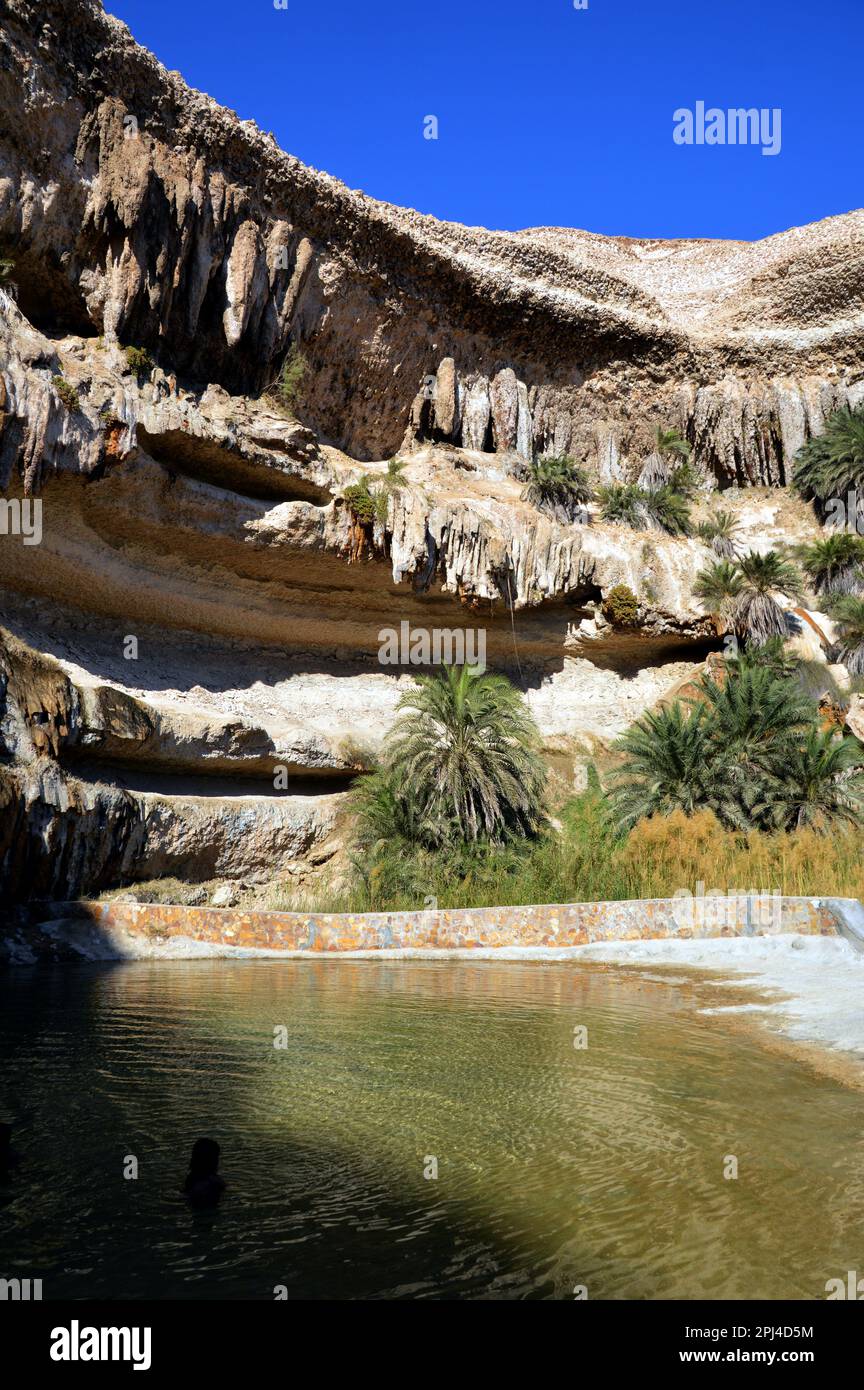 Oman:  an oasis in Wadi Shuwaymiyah, the pool backed by limestone cliffs with bizarre stalactites and caves and fringed with palm trees. Stock Photo