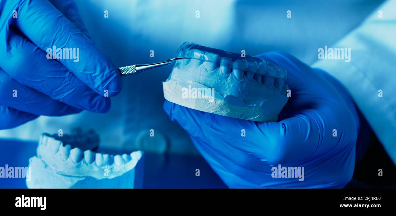 a technician, wearing blue latex gloves, adjusting an occlusal splint, in a panoramic format to use as web banner or header Stock Photo