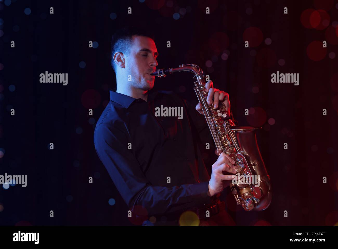 Young man playing saxophone on dark background. Bokeh effect Stock Photo