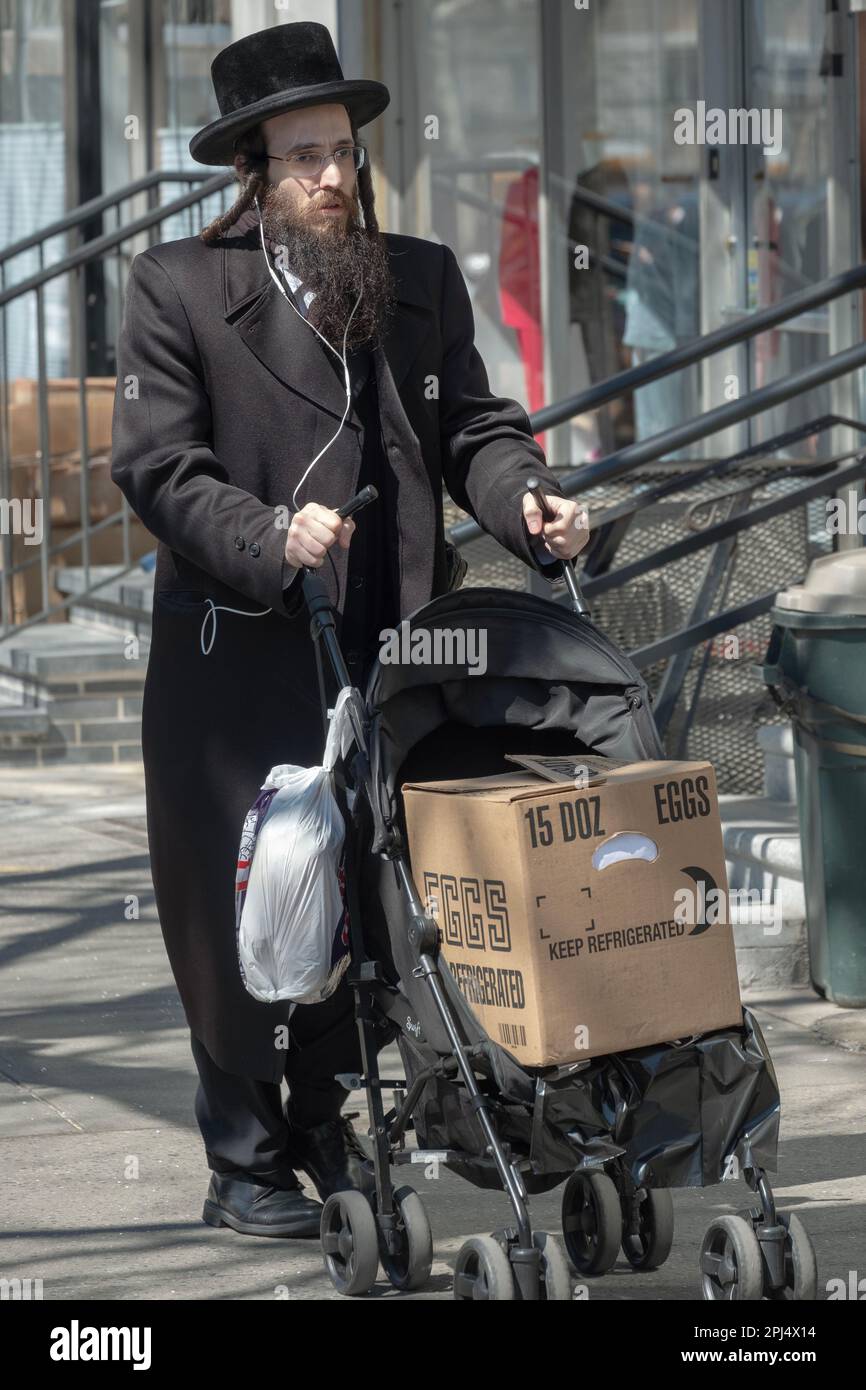 A Hasidic Jewish man with long peyot shops and uses a baby stroller to take a heavy box home or to his car. In Brooklyn, New York City. Stock Photo