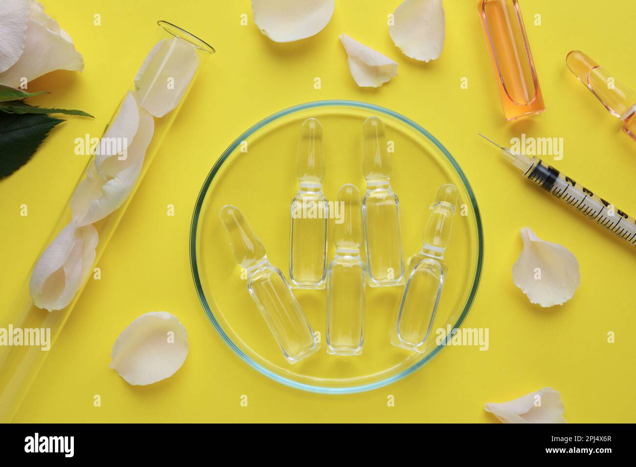 Pharmaceutical ampoules with medication, petals and syringe on yellow