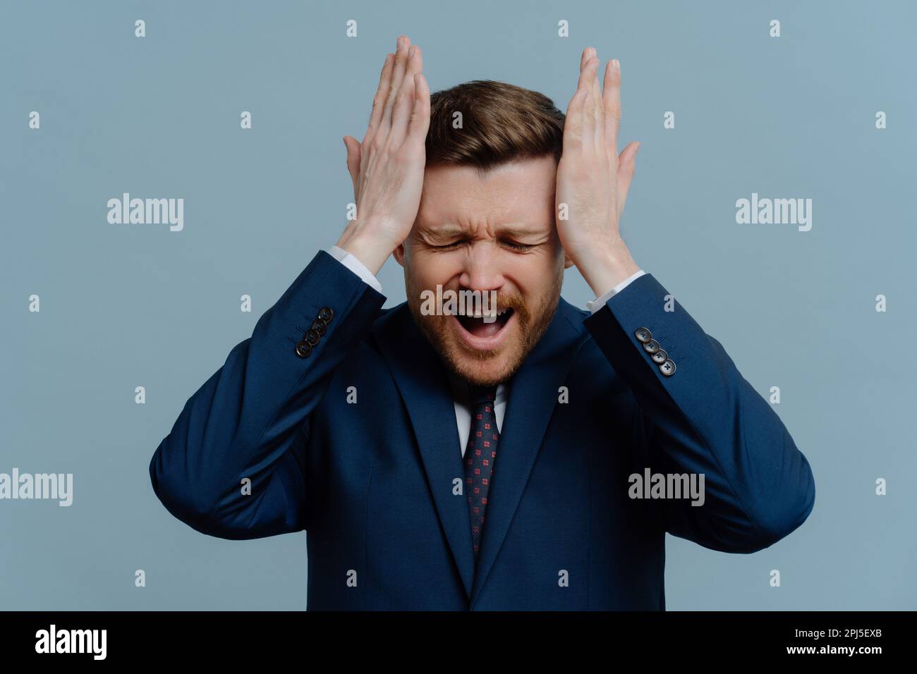 Business failure. Unhappy frustrated businessman or male entrepreneur wearing suit keeping head in hands and screaming loudly from receiving bad negat Stock Photo