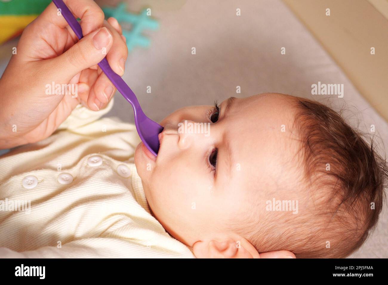 Newborn child drinking water or medicine cough syrup with spoon, close