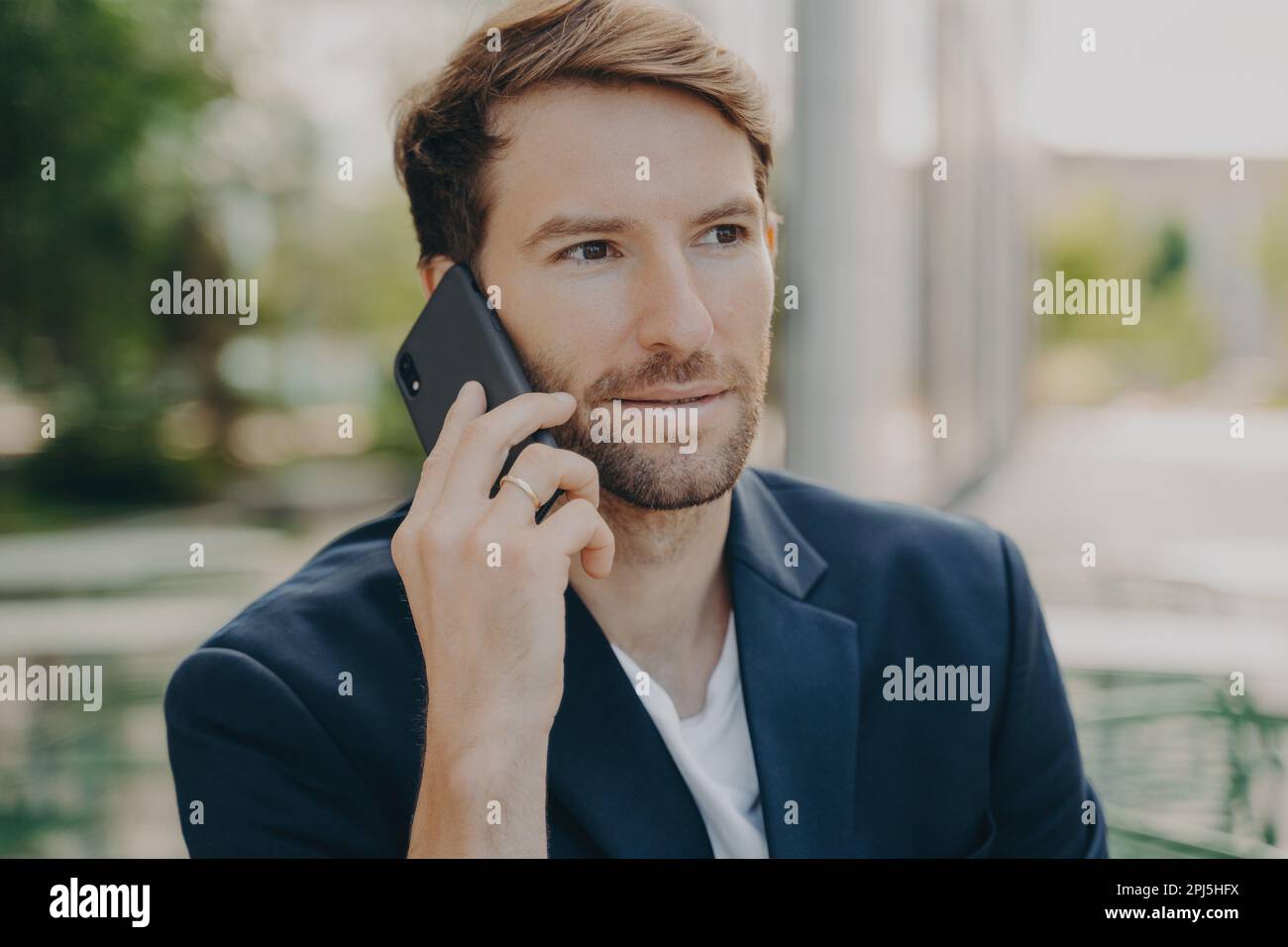 Horizontal shot of male entrepreneur or manager consults client by telephone call discusses future project has self confident expression poses outdoor Stock Photo