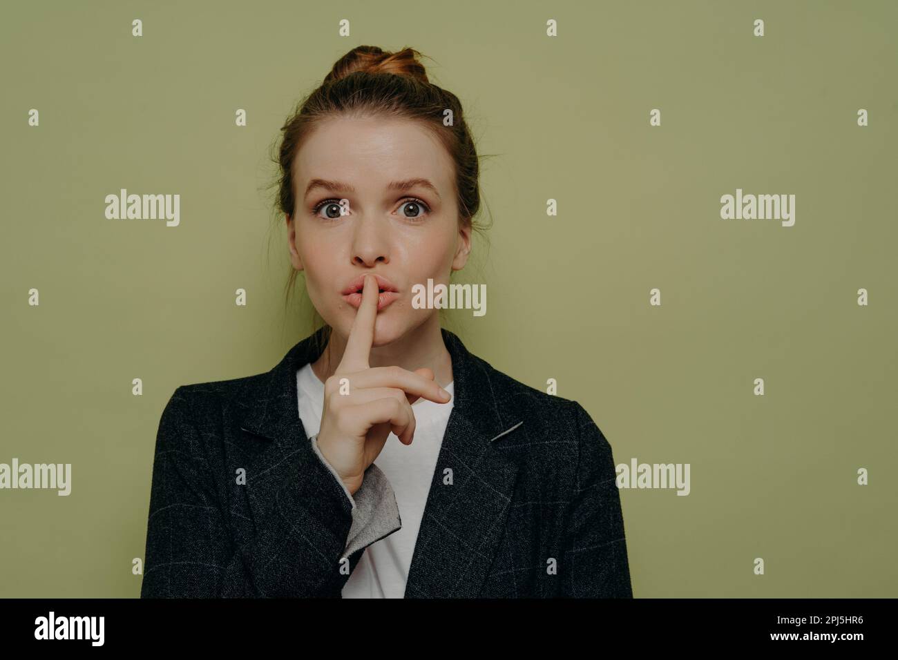 Mysterious young woman in casual wear asking to be quiet or keep something in secret, young female making shushing or silence gesture with finger on l Stock Photo