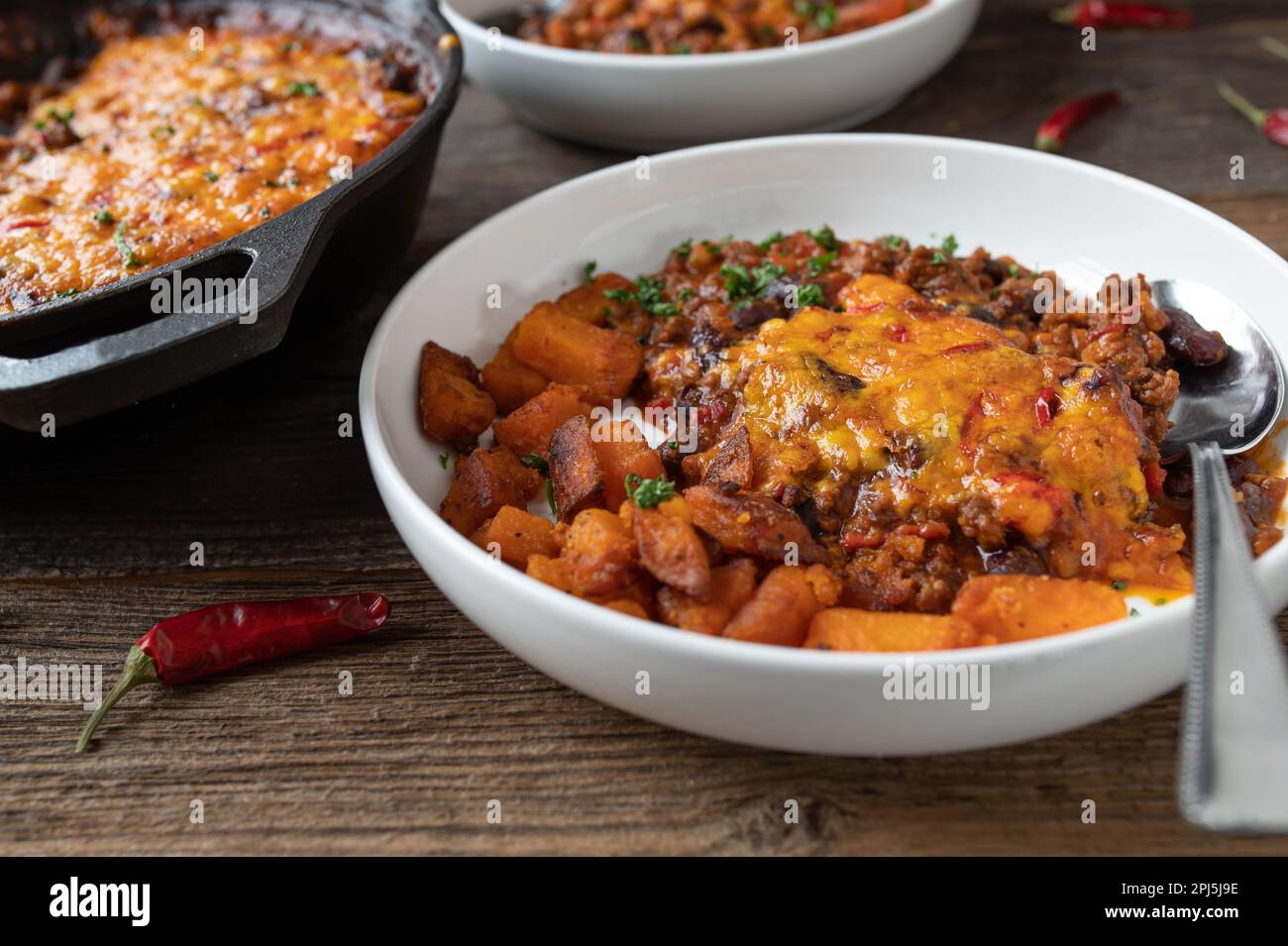 Bean stew with ground beef and gratinated cheddar cheese topping and roasted sweet potatoes Stock Photo