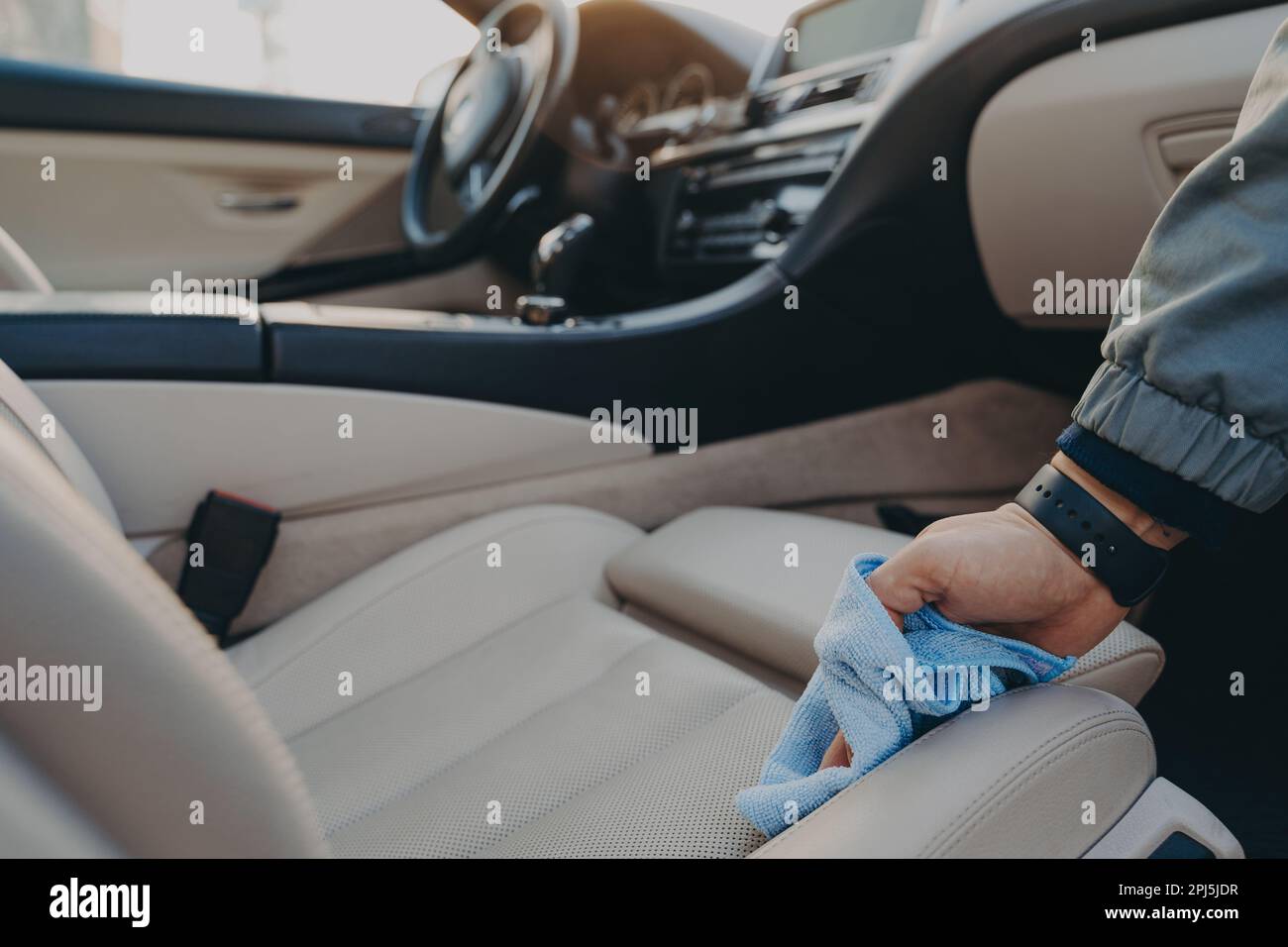 Cropped shot of man cleaning car interior, wiping fabric passenger seat