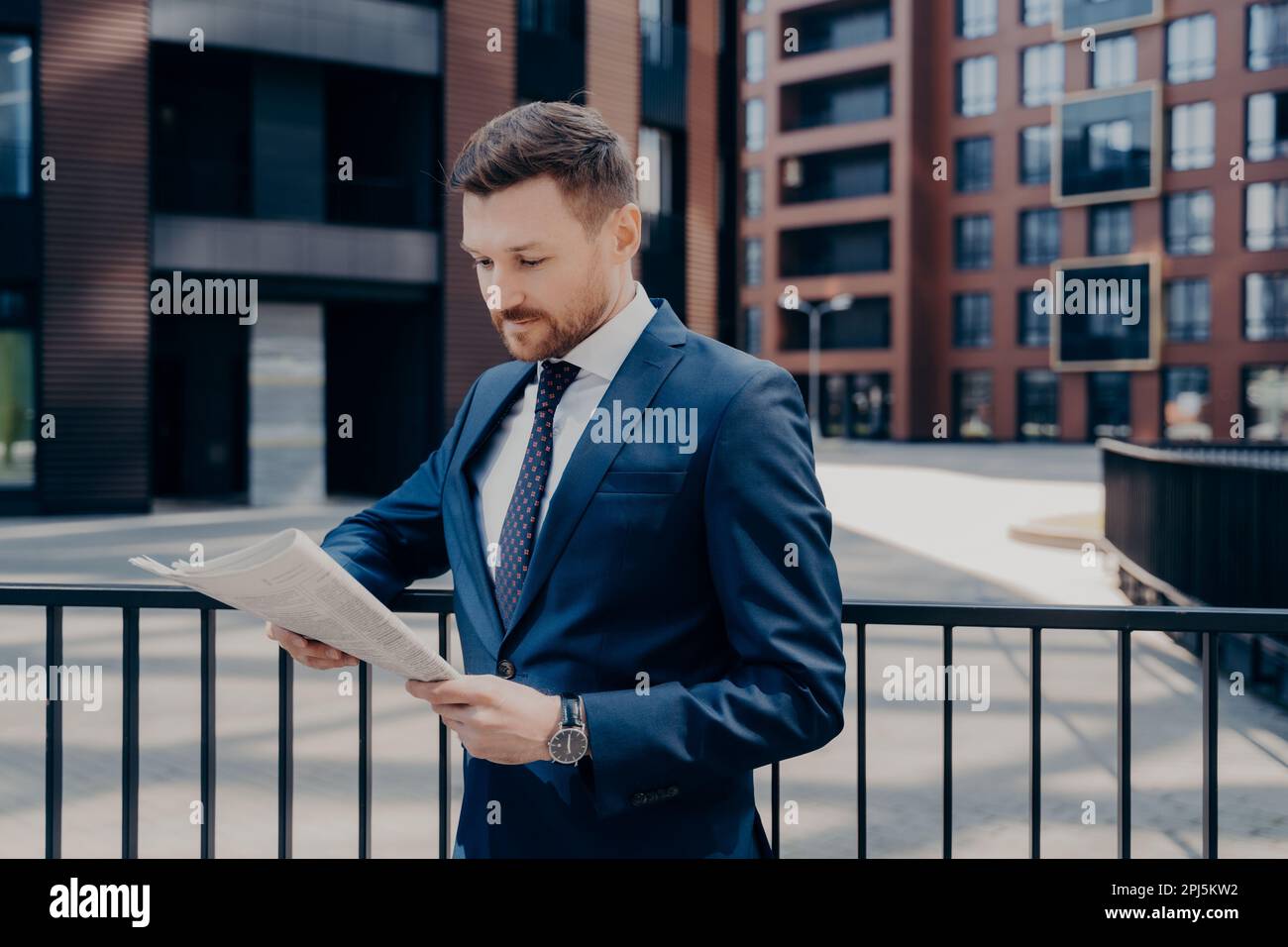 Confident proud CEO dressed in elegant wear reading business publication on early morning while walking along office centre outside, successful entrep Stock Photo