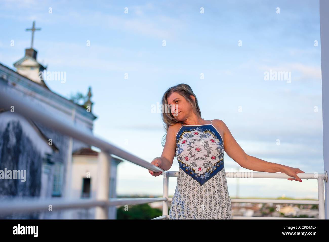 Beautiful woman standing on porch of home. in the background the sky and clouds. Stock Photo