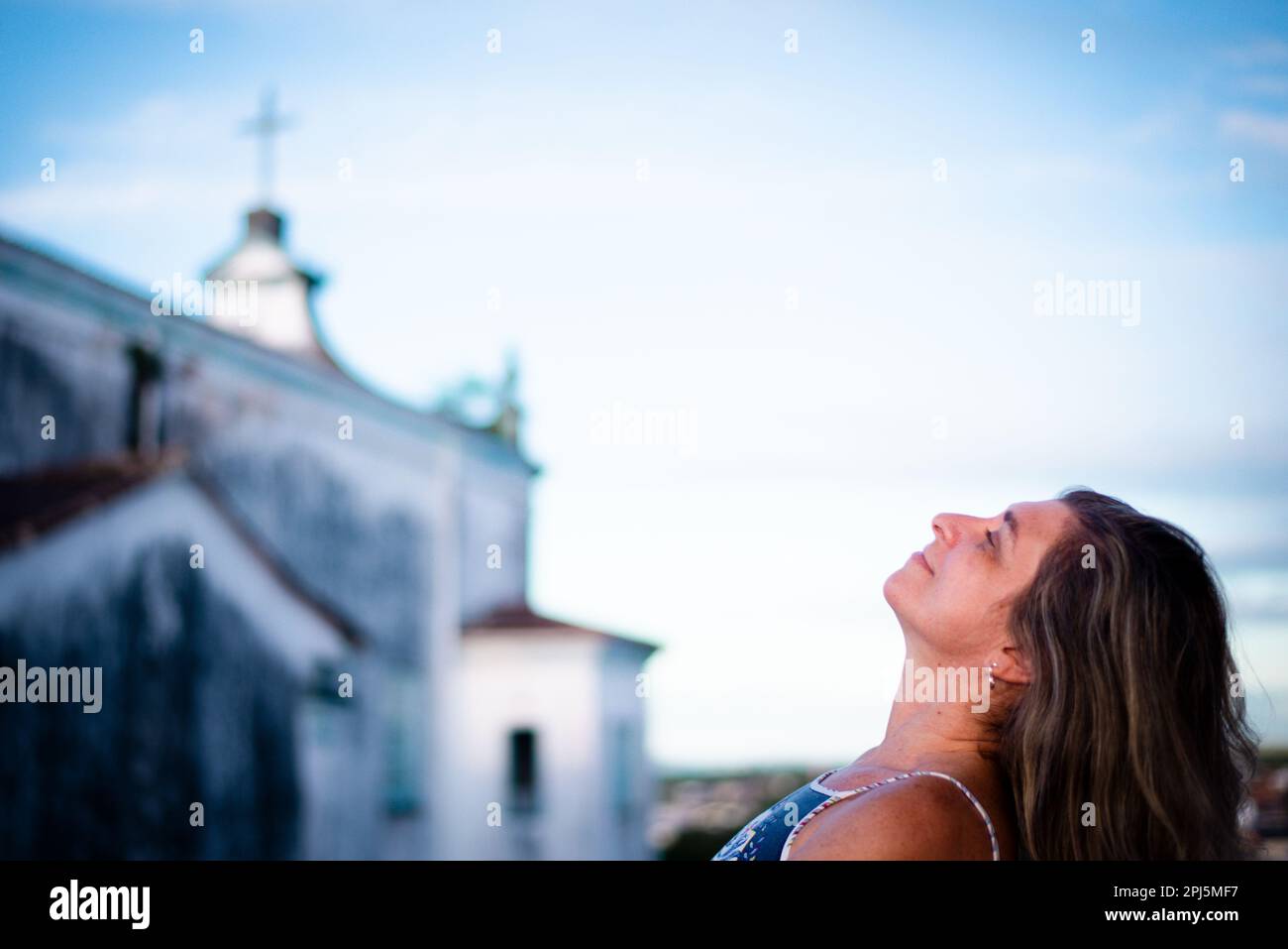 Beautiful woman on porch of home looking up. in the background the sky, clouds and a church. Stock Photo