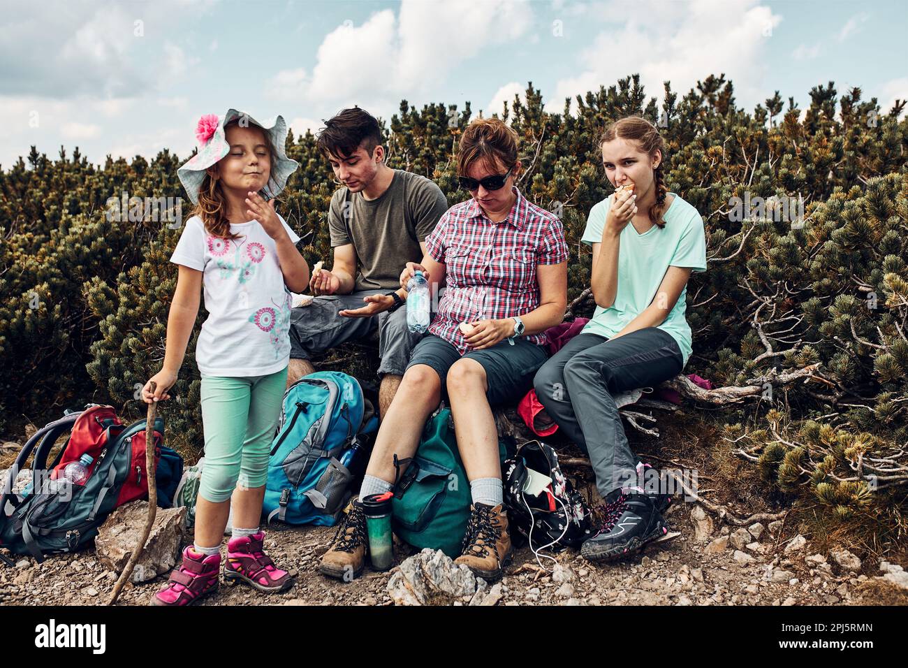 Family having break and eating snacks during trip in mountains. Family actively spending summer vacation together. Mother with her children teenagers Stock Photo