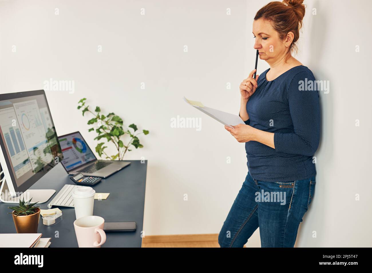 Woman entrepreneur focused on solving difficult work. Confused businesswoman thinking hard holding doccuments standing at her desk in office Stock Photo