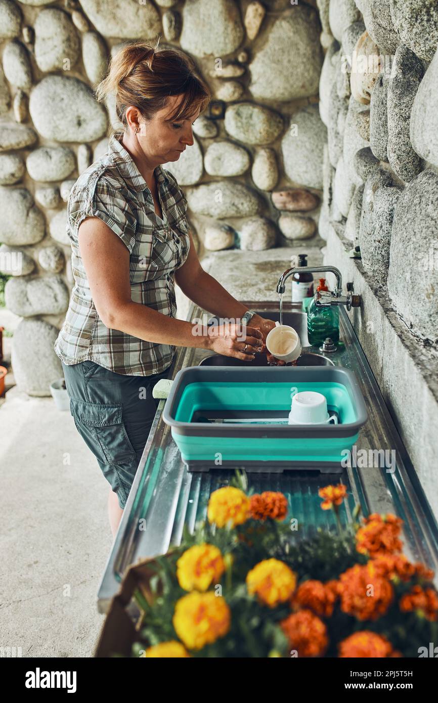 Woman washing up the dishes pots and plates in the outdoor kitchen during vacations on camping. Camp life Stock Photo