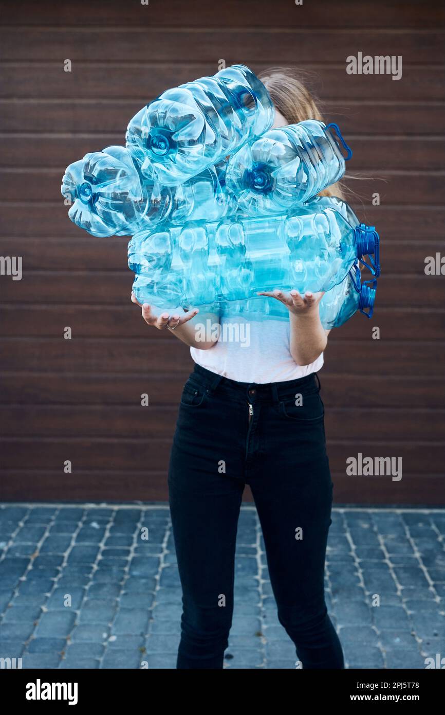 Young woman throwing out empty used plastic water bottles into trash bin. Collecting plastic