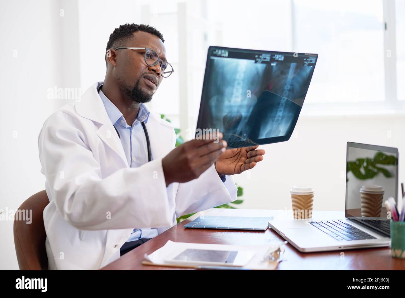 Serious looking Black doctor holds x ray to diagnose patient in office Serious looking Black doctor holds x ray to diagnose patient in office