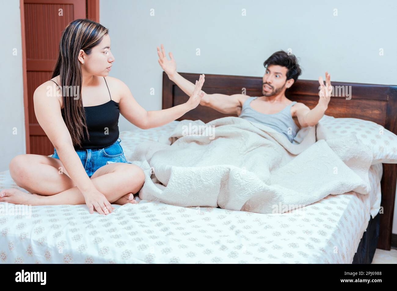 Upset woman with husband in bedroom bed, Husband fighting with his wife in bed. Young couple arguing in bed room. Concept of couple problems in bed Stock Photo