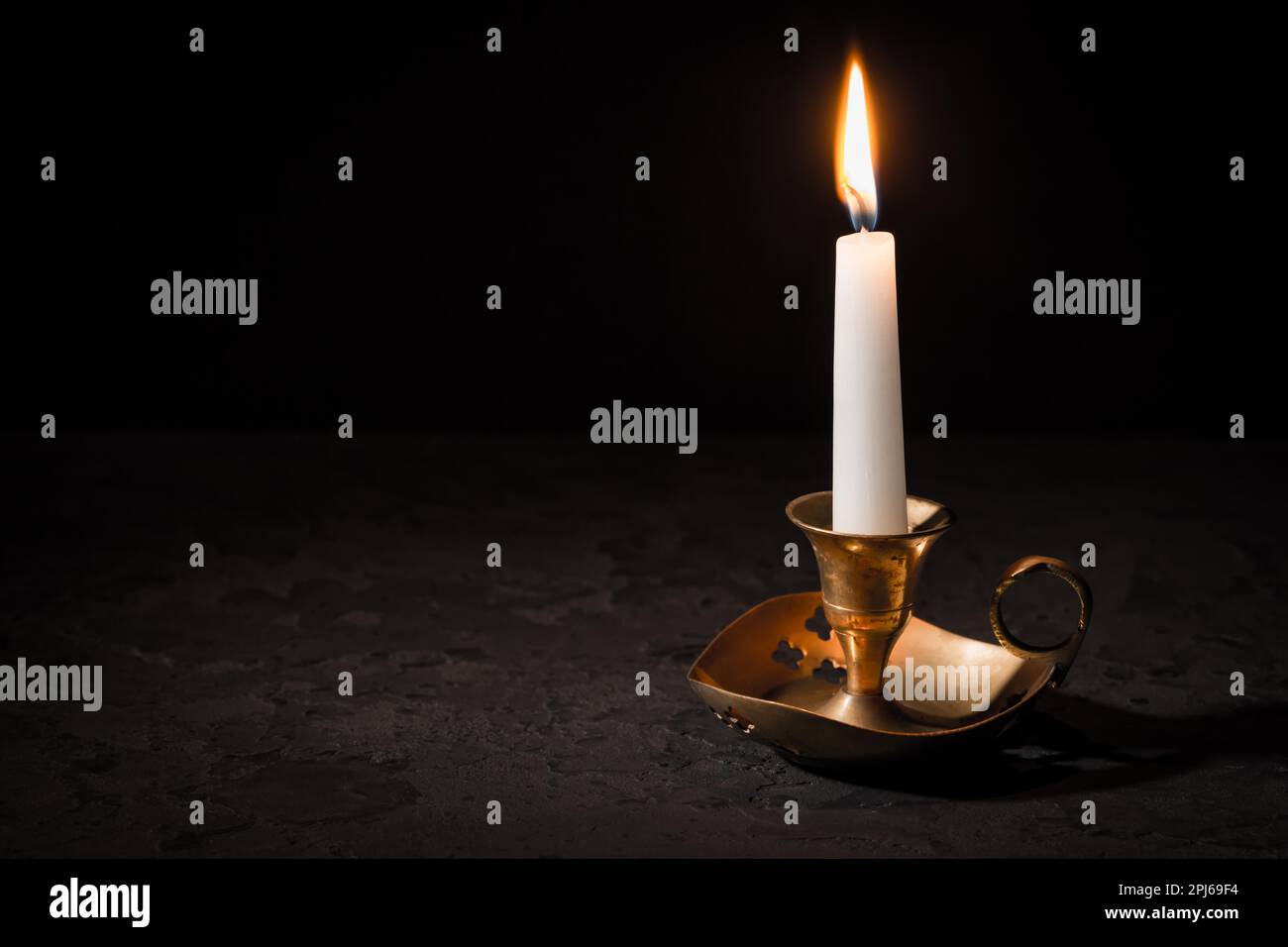 Burning candle in vintage candlestick on black background. Copy space ...