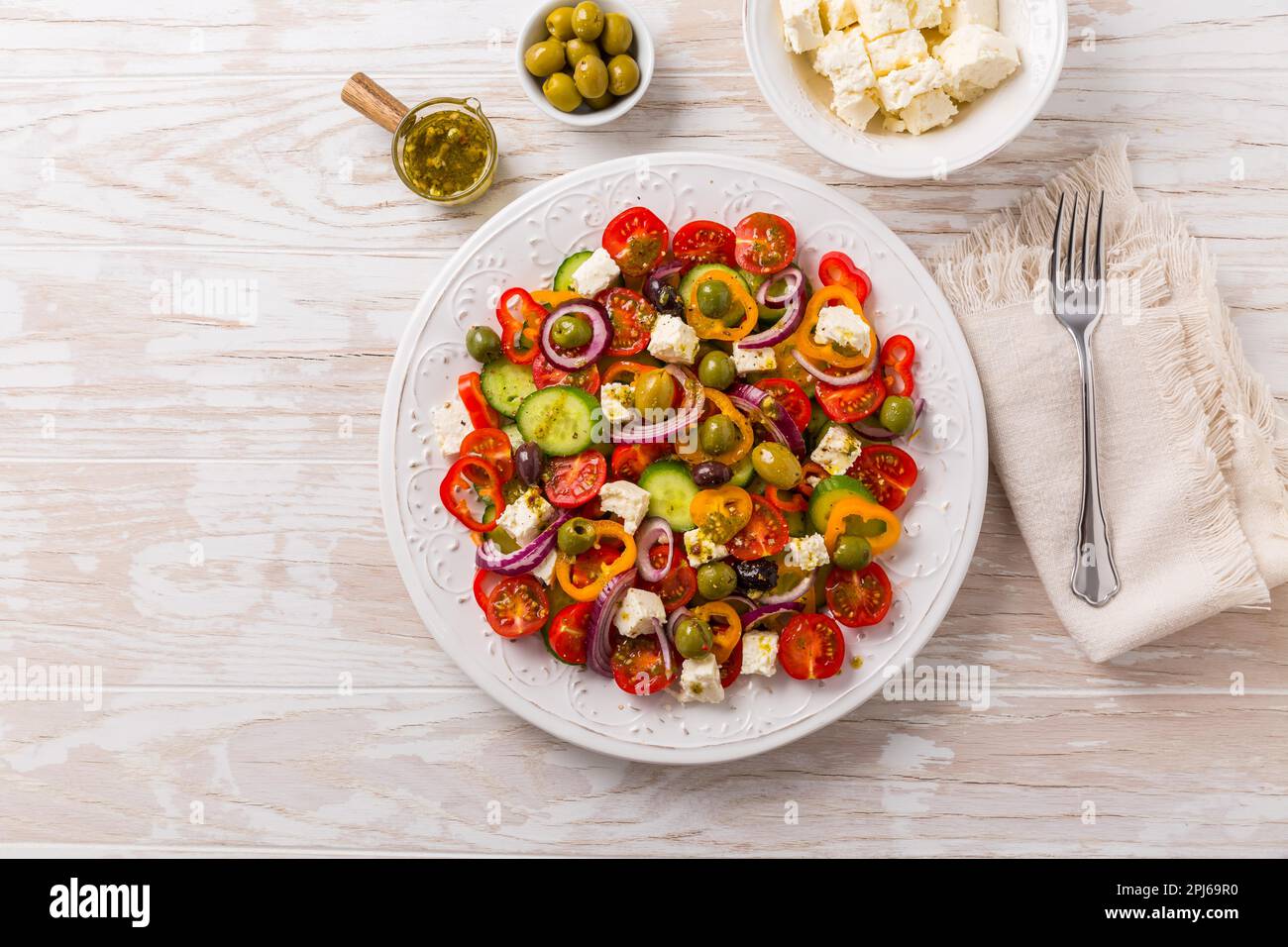 Greek salad of fresh cucumber, tomato, sweet pepper, lettuce, red onion, feta cheese and olives with olive oil dressing. Healthy food, top view Stock Photo